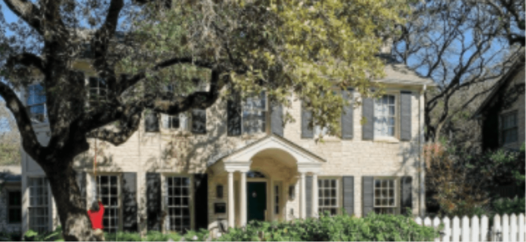 A traditional two-story stone house with dark shutters and a green door, framed