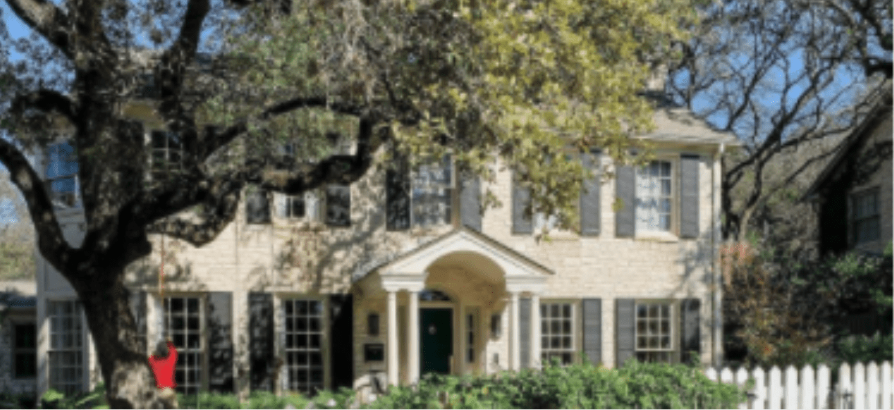 A traditional two-story stone house with dark shutters and a green door, framed