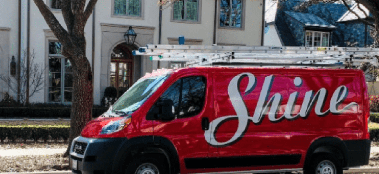 A red Shine service van with ladders on its roof is parked outside a large, upscale residence