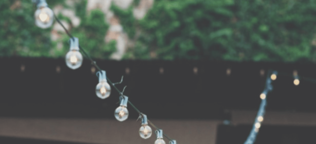 A string of glowing globe lights hangs diagonally with a blurred green and dark background. TITLE: