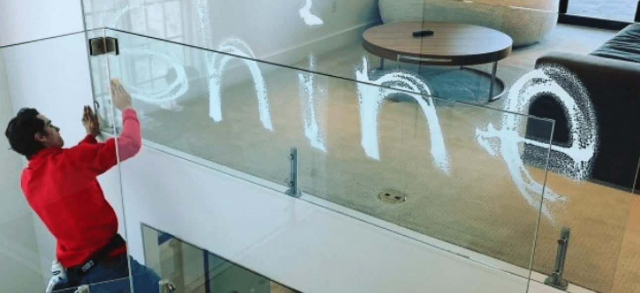A man in a red shirt cleans a glass railing, spelling "online" with white
