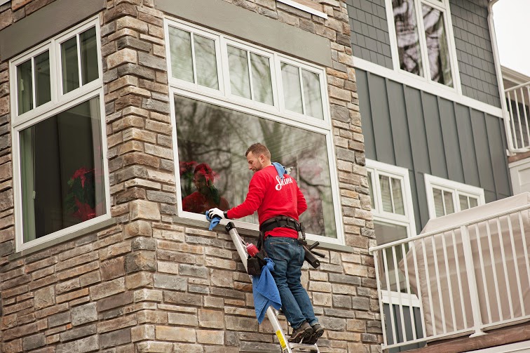 A man in a red shirt cleans a large window on a stone-clad building while