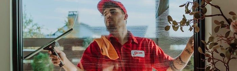 A professional window cleaner in a red uniform and cap uses a squeegee on a