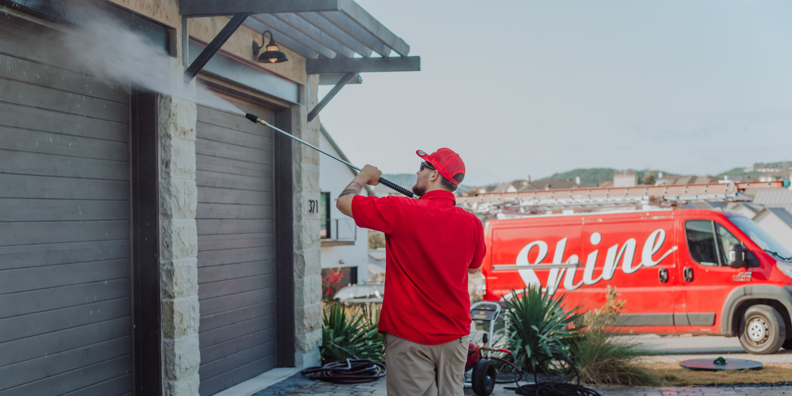 A professional in a red uniform pressure washes a modern house's garage door with a red