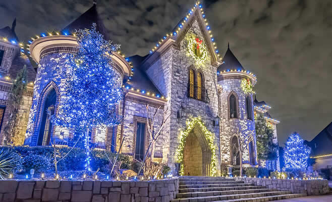 Castle-like stone home adorned with bright blue and warm white holiday lights at night.