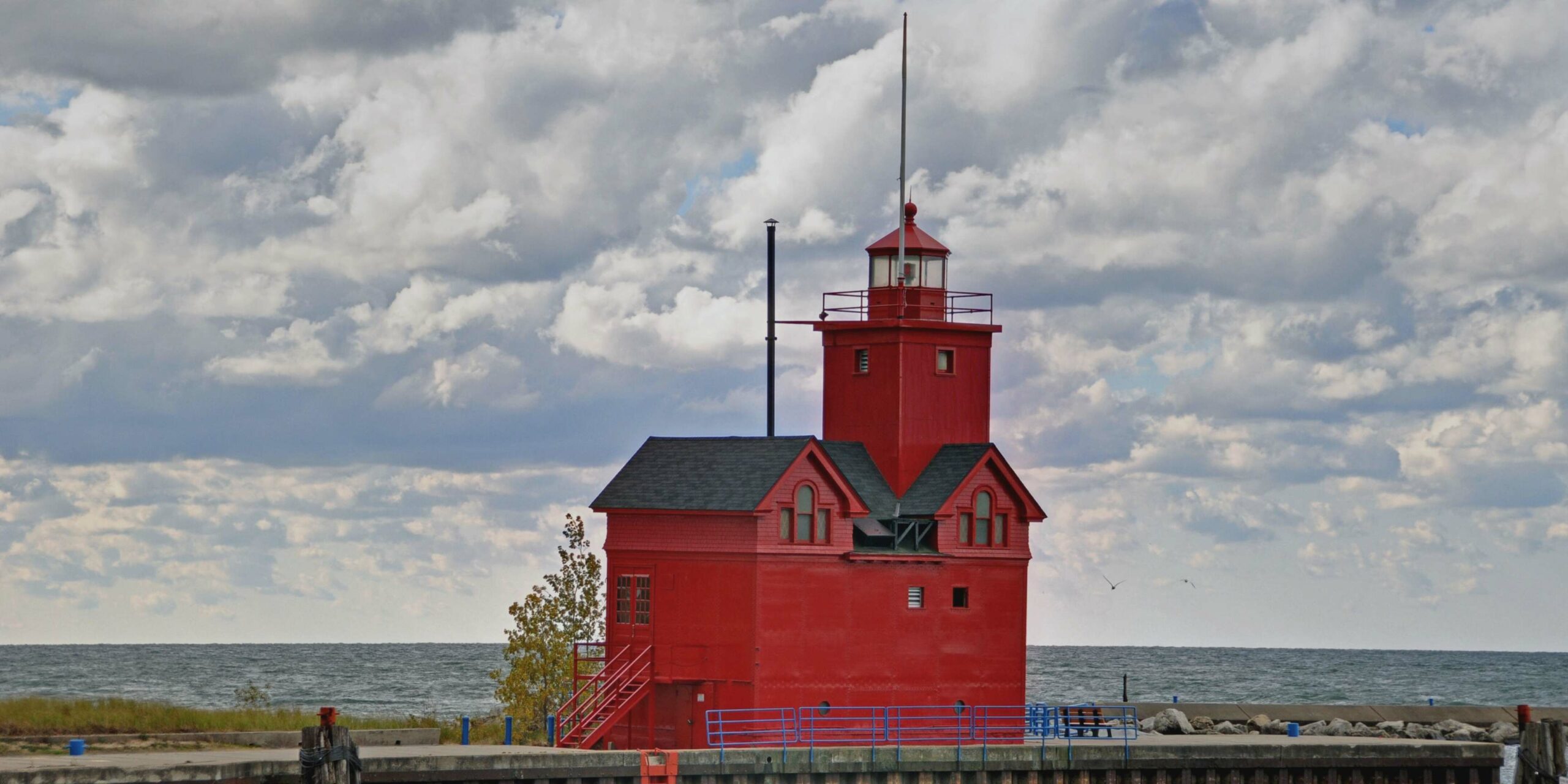 A distinctive red lighthouse, known as Big Red, stands on a pier against a cloudy sky and