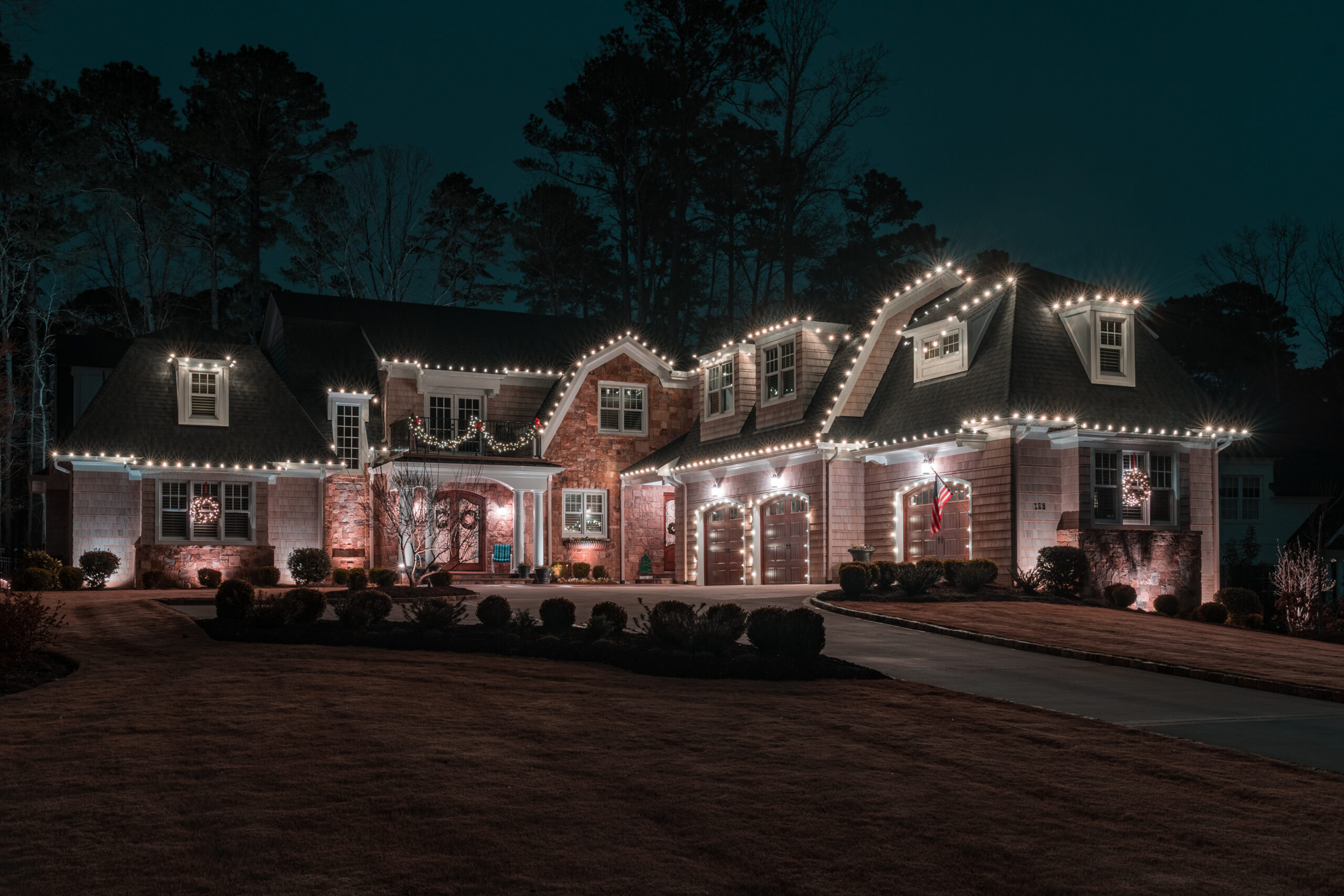 Elegant house decorated with warm white string lights outlining its roof, dormers, and garage