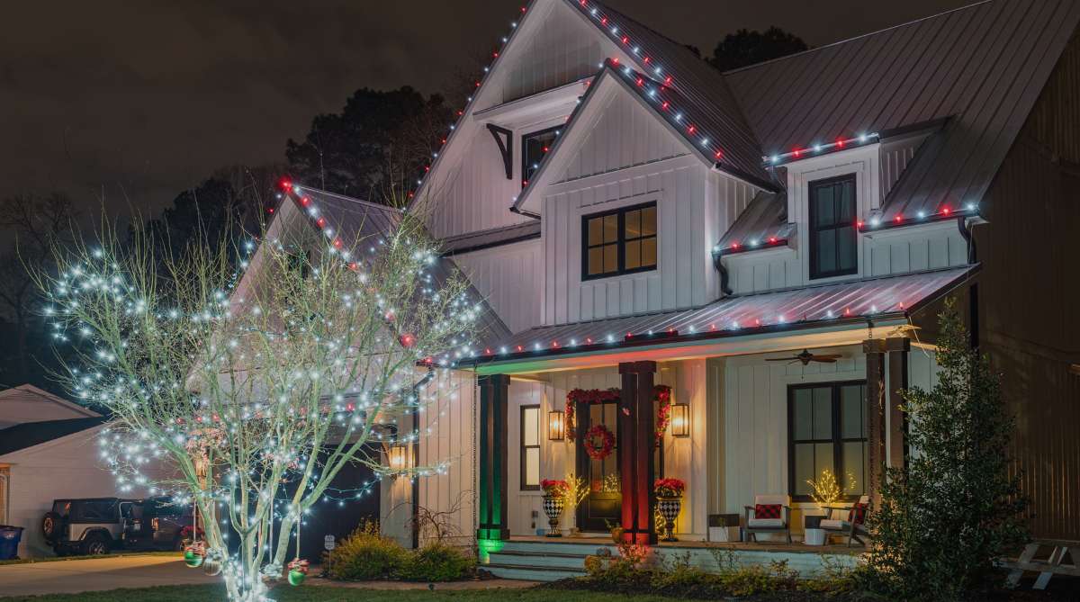 Modern white farmhouse decorated with red and white Christmas lights and a brightly lit tree at