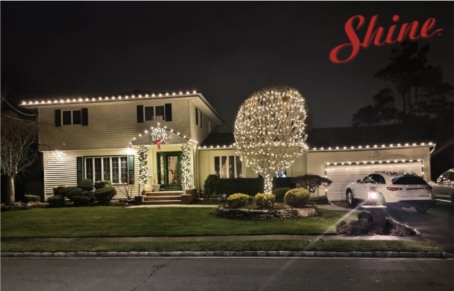 Beautifully decorated house and tree glow with warm white holiday lights at night.