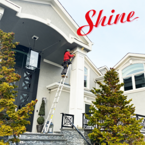 Shine employee on a ladder installing permanent lighting with Shine branding.