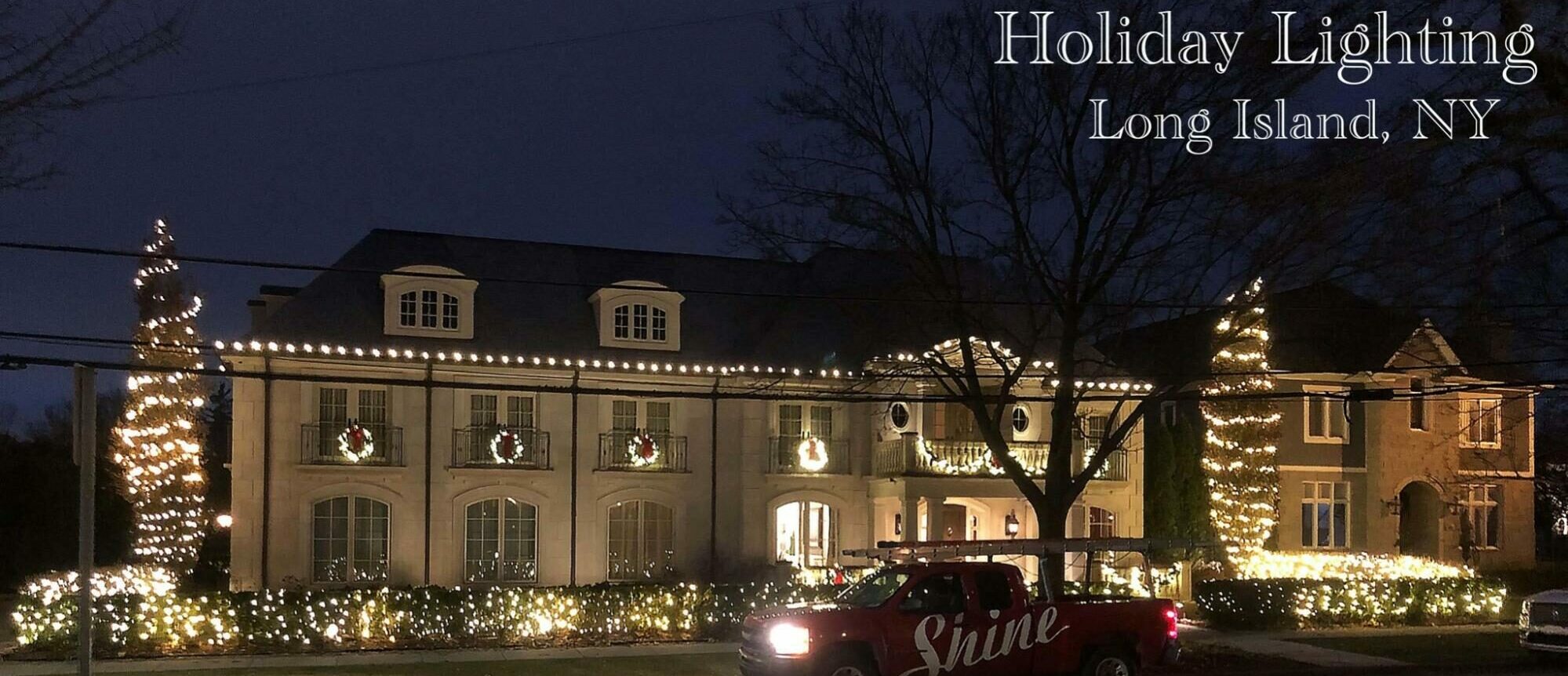 A large Long Island house glows with festive holiday lights at night, with a Shine lighting truck parked