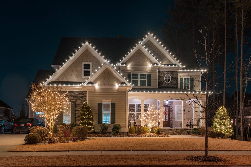 Suburban house at night, professionally decorated with warm white Christmas lights.