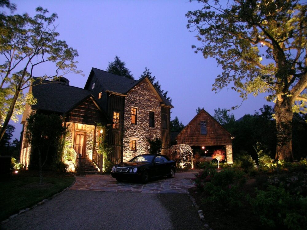 Luxurious stone and wood house beautifully illuminated by warm outdoor lighting at dusk.