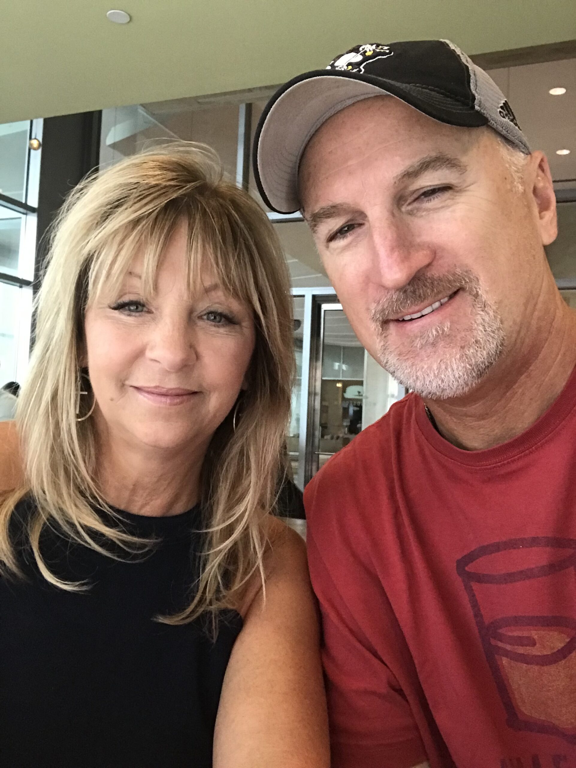 A smiling blonde woman and a man in a baseball cap take a selfie. TITLE