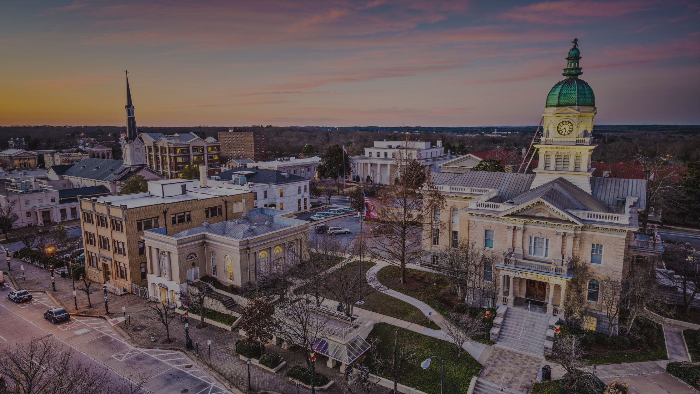 Aerial view of a historic town square with a courthouse and green dome at sunset. TITLE