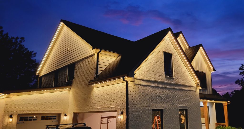 A modern white house is beautifully illuminated by warm accent lights along its rooflines at