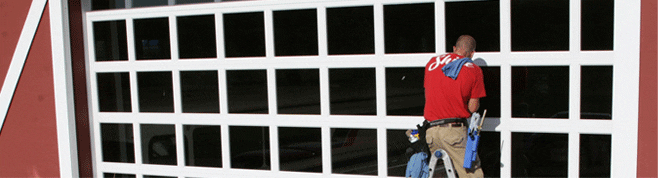 Shine employee in red shirt and khakis cleans square window panels on a garage door exterior