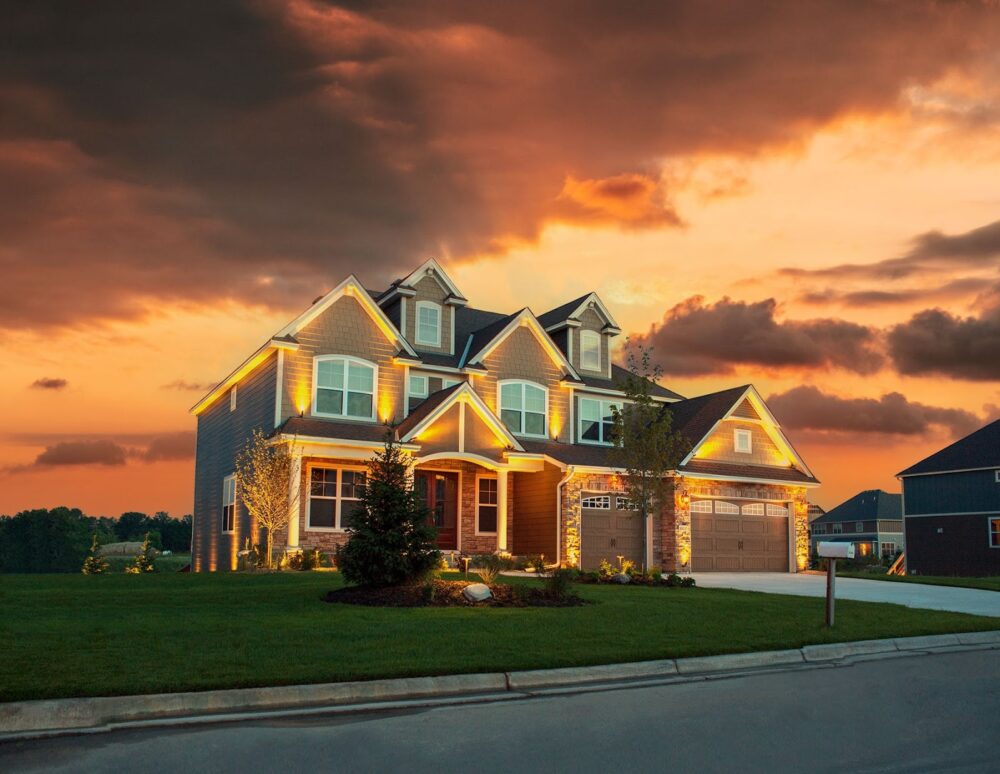 Modern suburban home with exterior lighting under a dramatic orange and cloudy sunset.