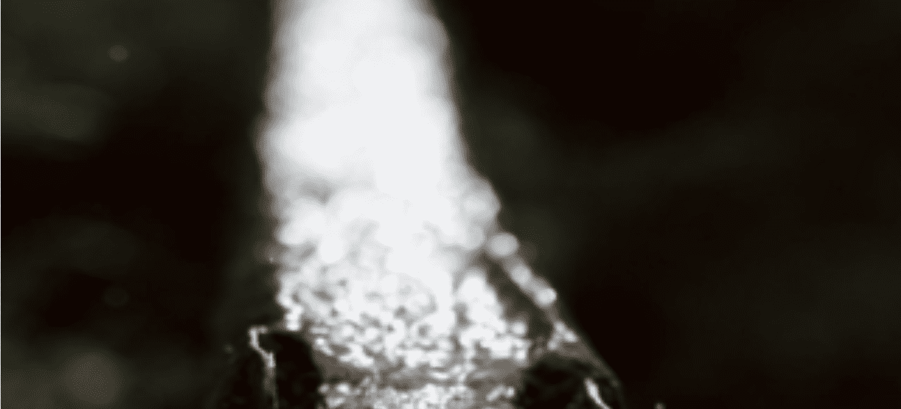A bright, frothy stream of water cascades downwards against a dark, blurry background.