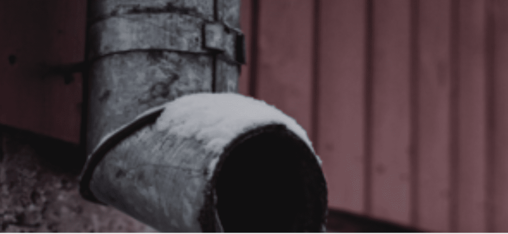 A weathered grey downspout with snow on its rim is attached to a dark red