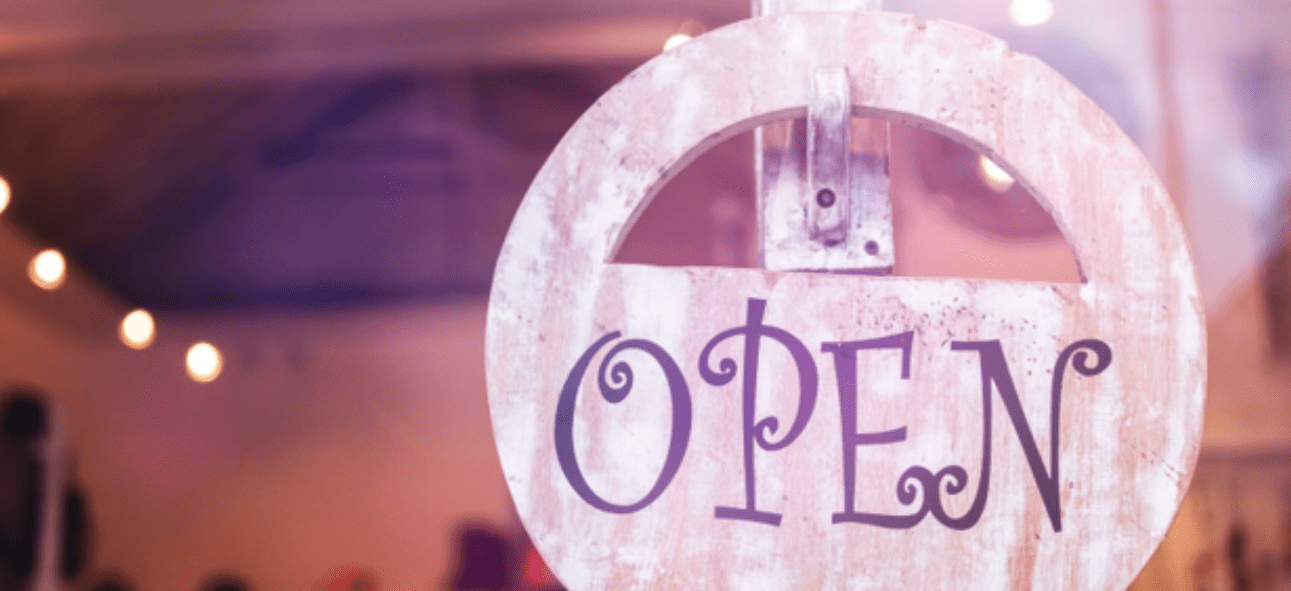 A rustic wooden "OPEN" sign hangs in a warm, inviting setting with blurred string lights.