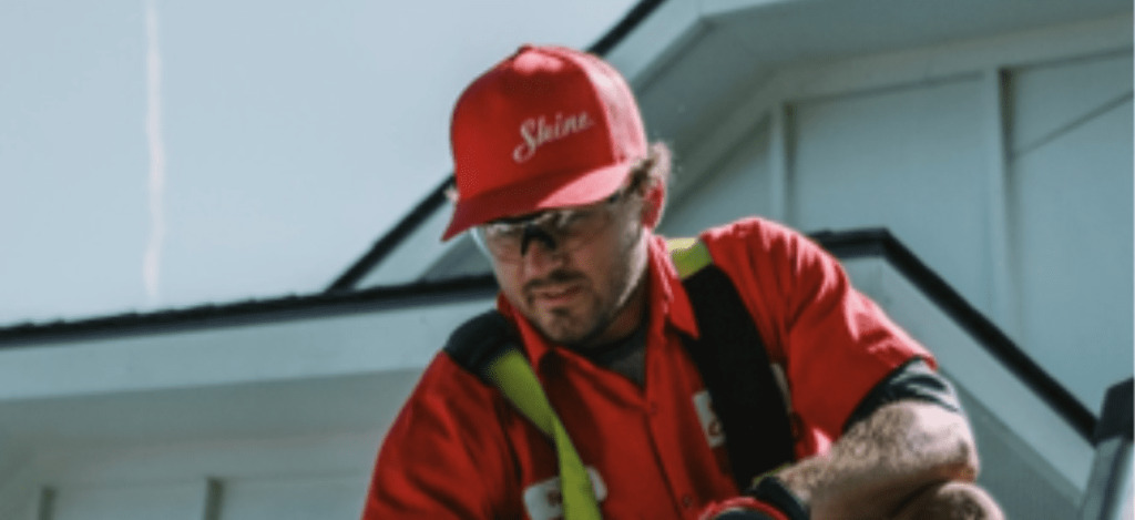 A service technician wearing a red "Shine" hat and safety glasses works on a