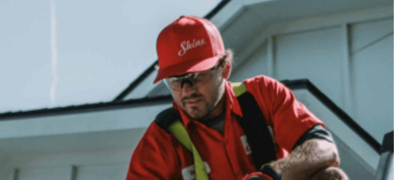 A service technician wearing a red "Shine" hat and safety glasses works on a