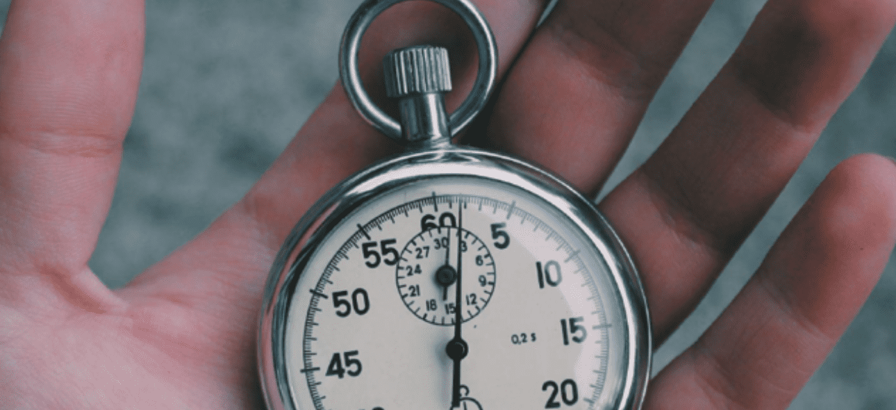 A hand holds a classic silver stopwatch with a white face and black numbers against a blurred background.