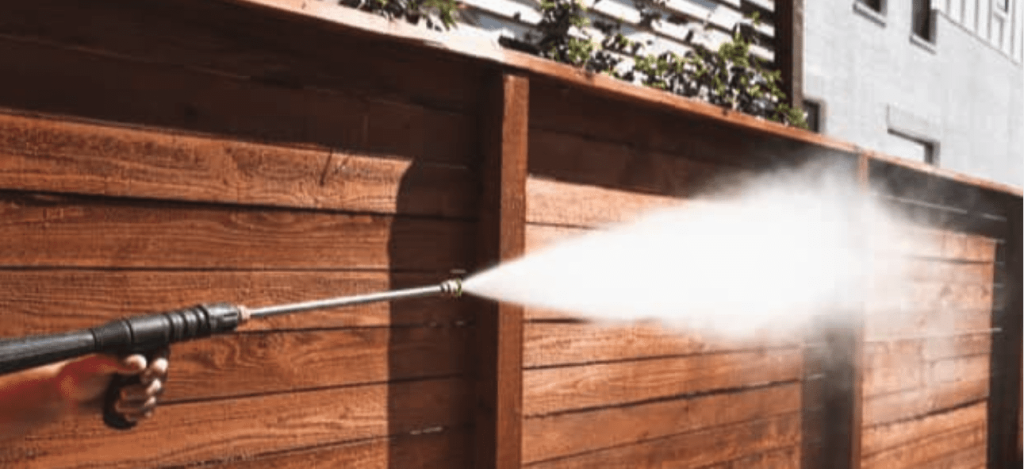 A hand operates a pressure washer, spraying a powerful stream of water onto a brown