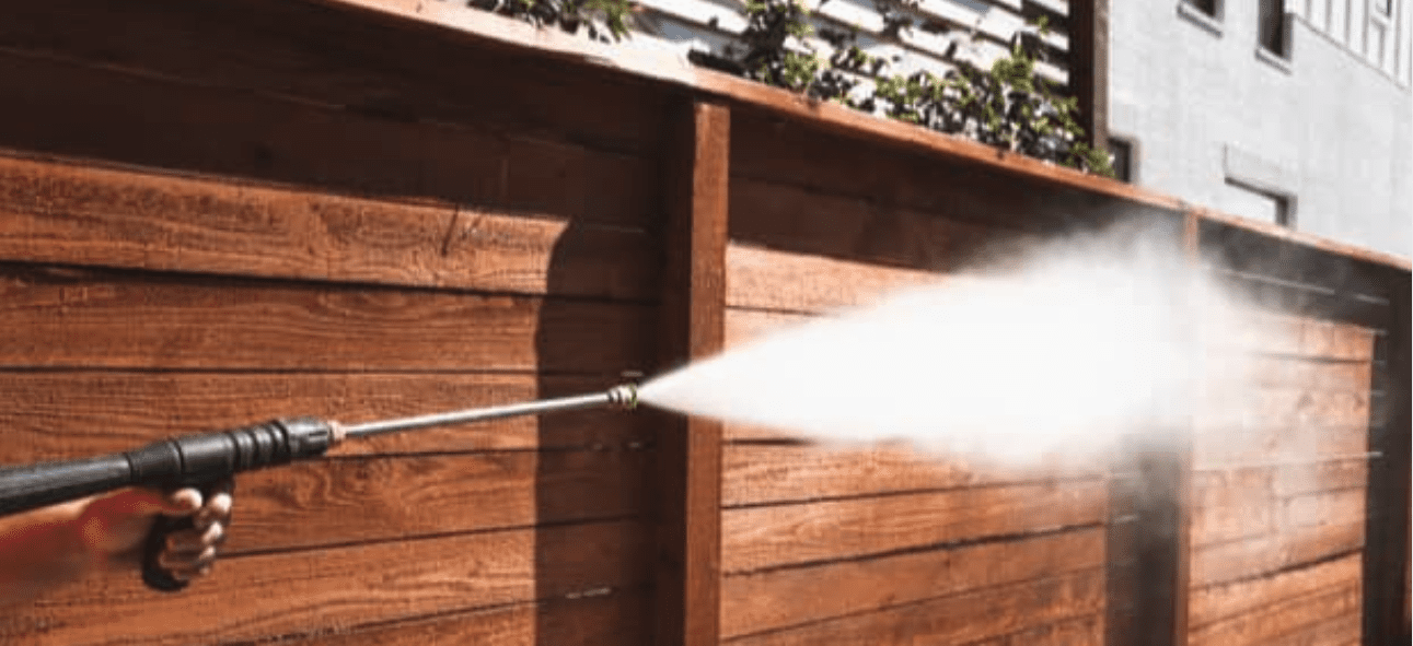 A hand operates a pressure washer, spraying a powerful stream of water onto a brown