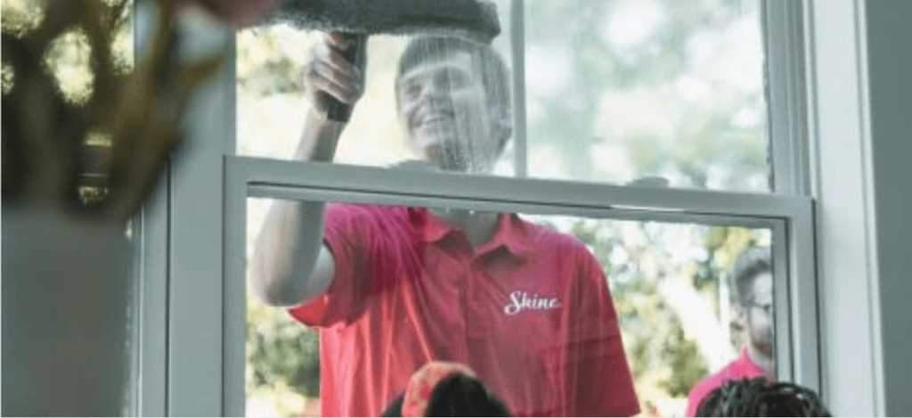 A smiling window cleaner in a red "Shine" shirt cleans a window with a