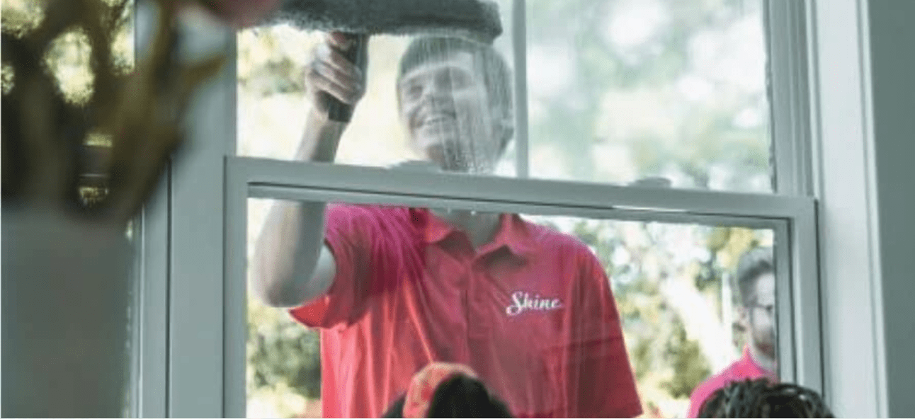 A smiling window cleaner in a red "Shine" shirt cleans a window with a