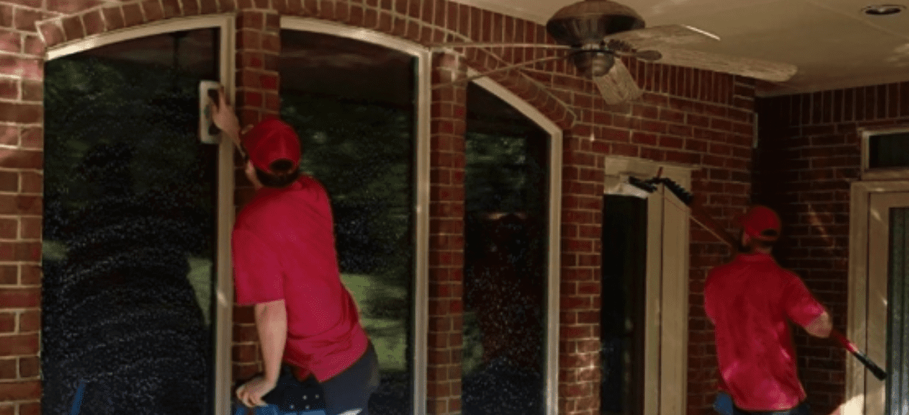 Two uniformed workers are diligently cleaning the sudsy windows of a brick building. TITLE