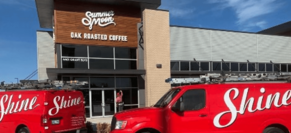 Two red Shine service vans are parked outside a modern Summer Moon Coffee shop.