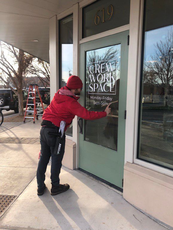 A person in a red jacket applies a "Crew Work Space" decal to a