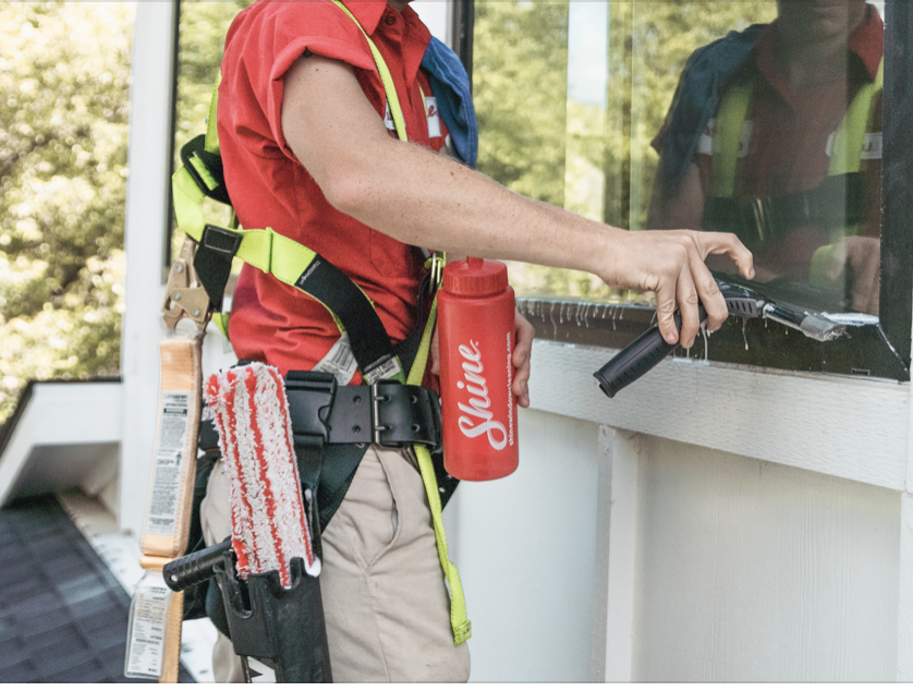 A professional window cleaner in a red shirt and safety harness cleans a window with a