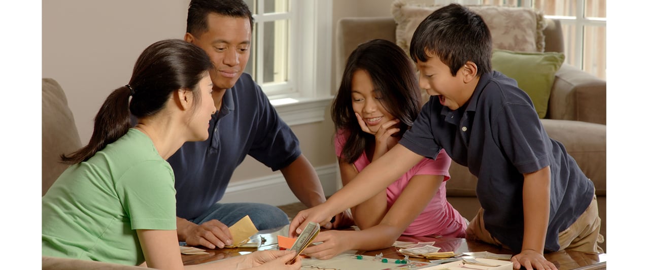 A happy Asian family, including two children, enjoys playing a board game together at home.