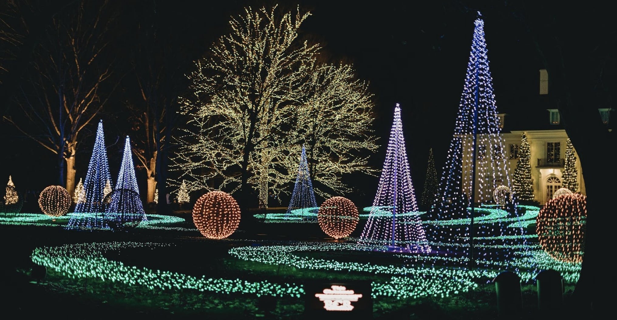 A dazzling outdoor display of colorful holiday lights illuminates trees, conical structures, and ground