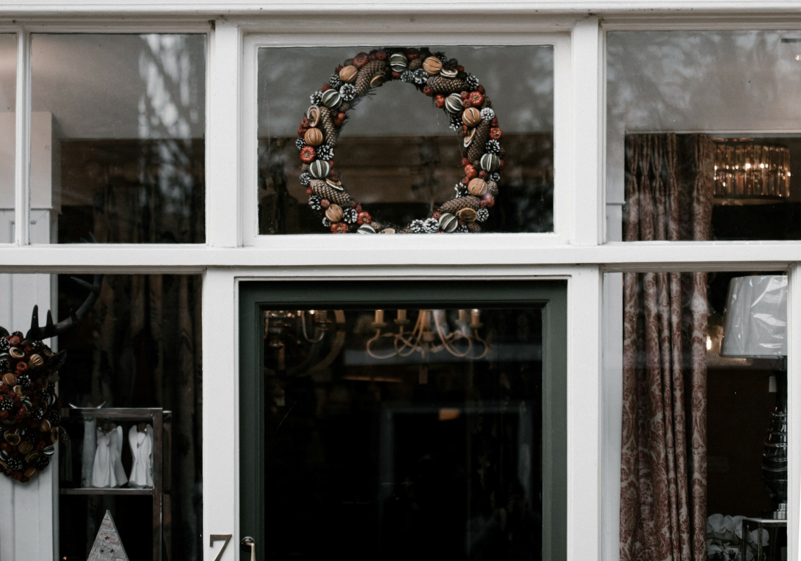 A colorful wreath made of pinecones, dried fruit, and berries adorns a window above