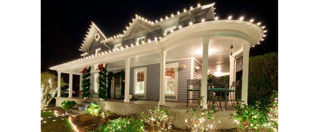 Beautiful white Christmas lights outline a charming house and its porch at night.
