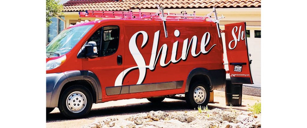 A bright red "Shine" window cleaning service van with ladders on its roof is parked
