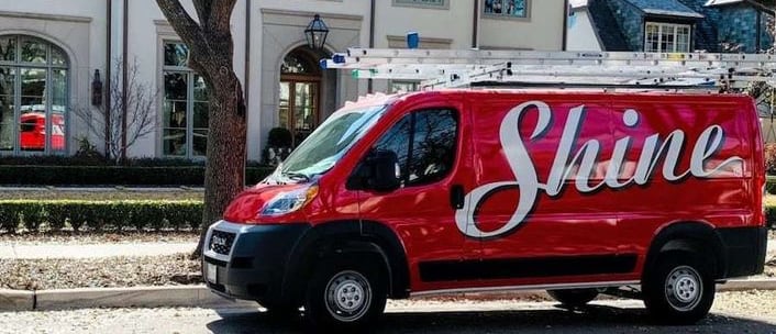 A red "Shine" service van with ladders on its roof is parked outside a luxurious home