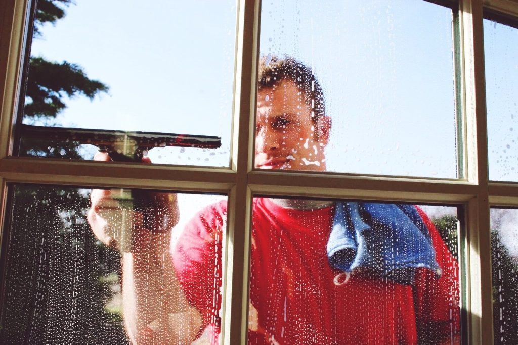 A man in a red shirt cleans a sudsy window with a squee