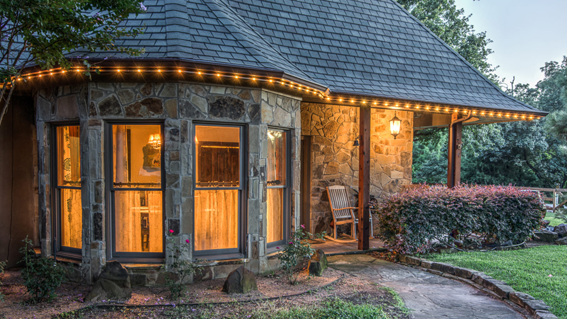 A charming stone house with a dark roof features glowing windows and decorative string lights at