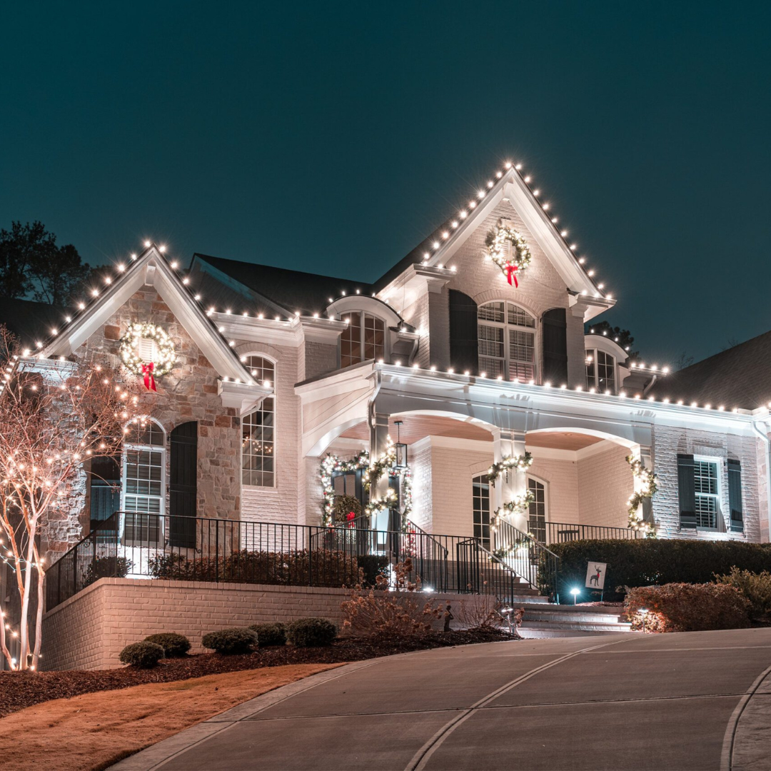 A large house is beautifully decorated with bright white Christmas lights and wreaths at night. TITLE: