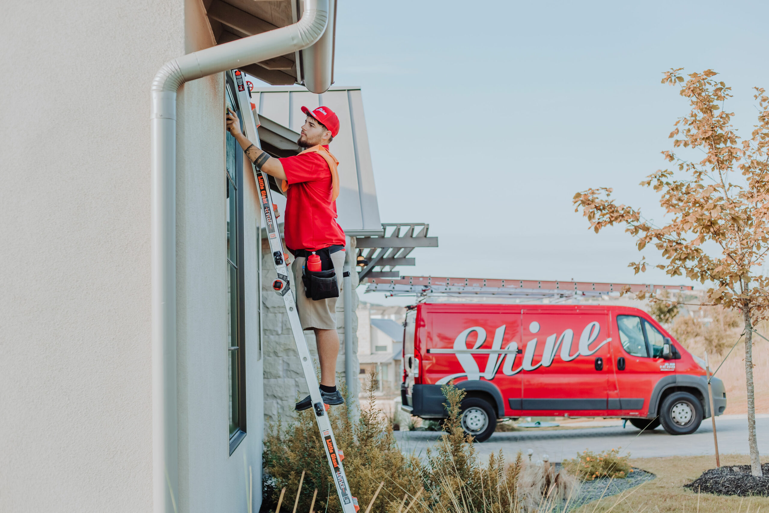 A service professional on a ladder cleans a window next to a red Shine van. TITLE: