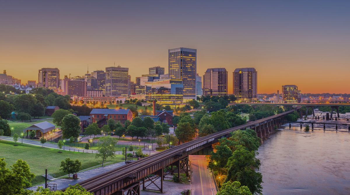 Richmond, Virginia skyline at dusk featuring the James River, railroad bridge, and illuminated buildings.