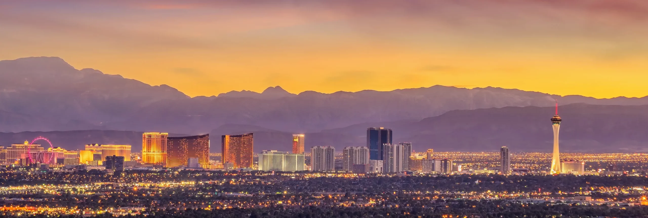 Las Vegas skyline glows at sunset with city lights, mountains, and the Stratosphere Tower.