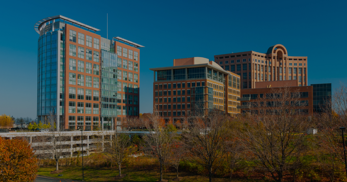Modern glass and brick office buildings stand under a clear blue sky, surrounded by autumn trees