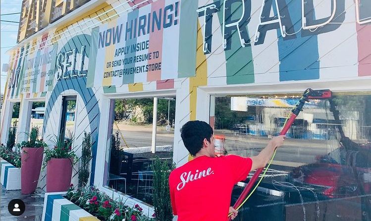 A person in a red "Shine" shirt cleans the large windows of a brightly